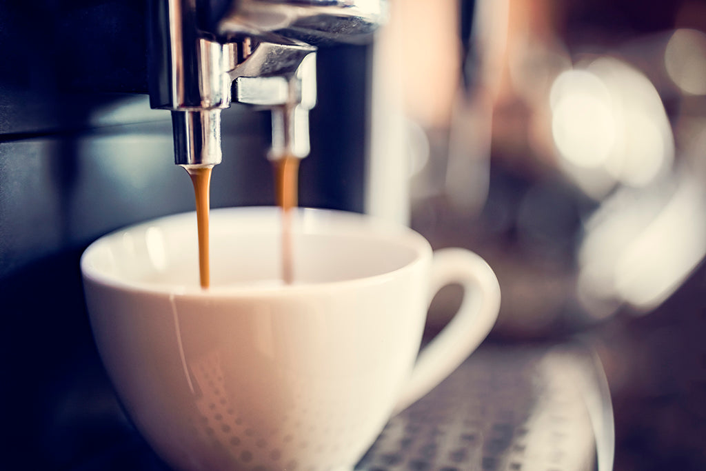 Espresso being poured from a machine into a white cup.